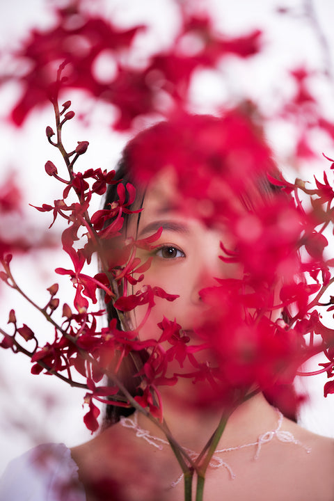 女性模特透過花卉之間的隙縫凝視前方,展現私密氛圍。