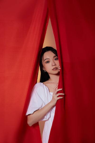 女性模特站於布簾後方,並掀開部分探出上半身,展現私密氛圍。