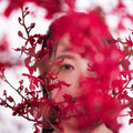 女性模特透過花卉之間的隙縫凝視前方，展現私密氛圍。